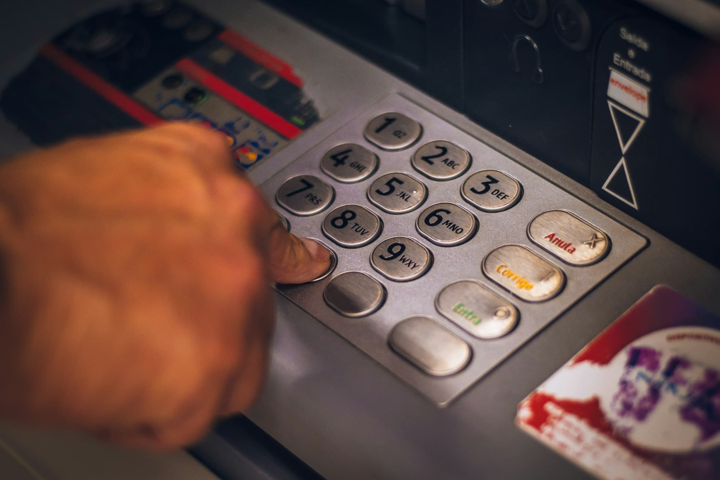A hand entering a PIN on an ATM keypad to withdraw cash